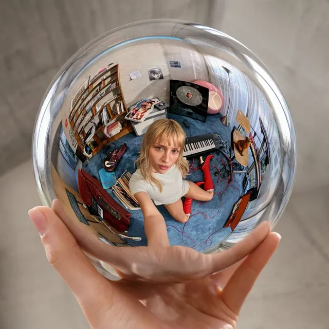 Pochette de l'album Instinct d'Angèle : la chanteuse assise dans une sphère de verre tenue par une main