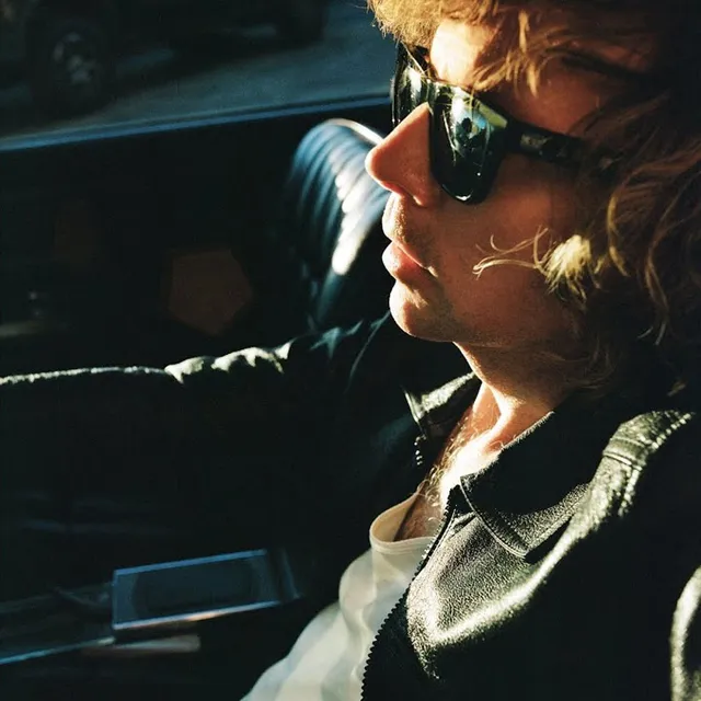 Pochette de l'album Ride Lonesome de Beck, l'artiste de profil, lunettes de soleil, dans une voiture au soleil couchant