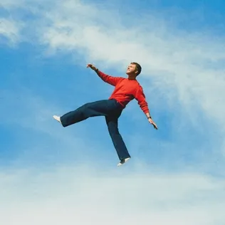 Pochette de l'album Wildchild d'Alex Warren : un homme en pull rouge saute dans un ciel bleu