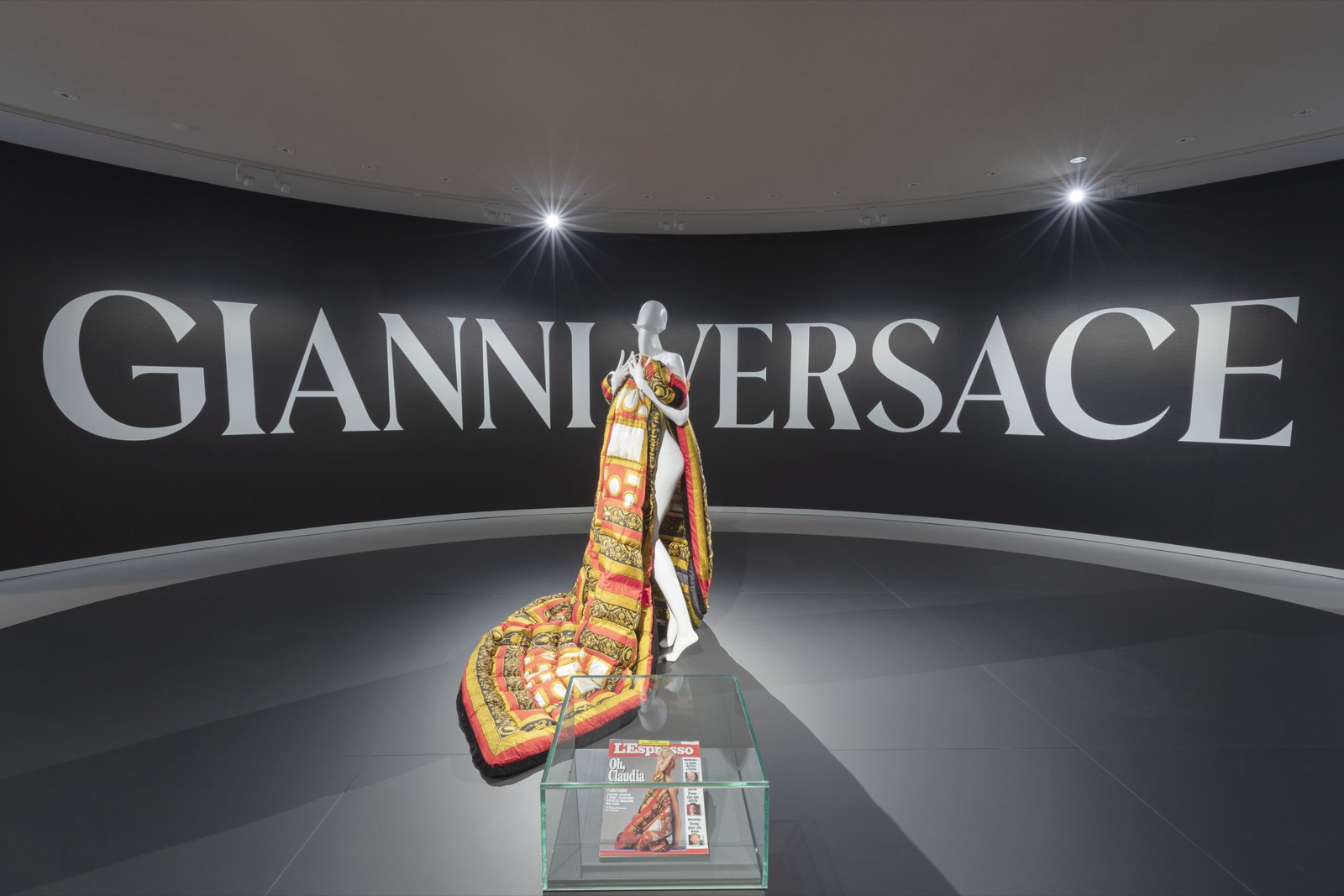 Vue de l'exposition Gianni Versace Retrospective au Musée Maillol, mannequin en cape baroque devant le nom du couturier