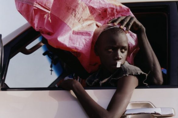 Tirage de Harley Weir presente a l'exposition Fragile Beaute au Jeu de Paume : un jeune passager a la fenetre d'une voiture, un grand sac rose pose sur la tete