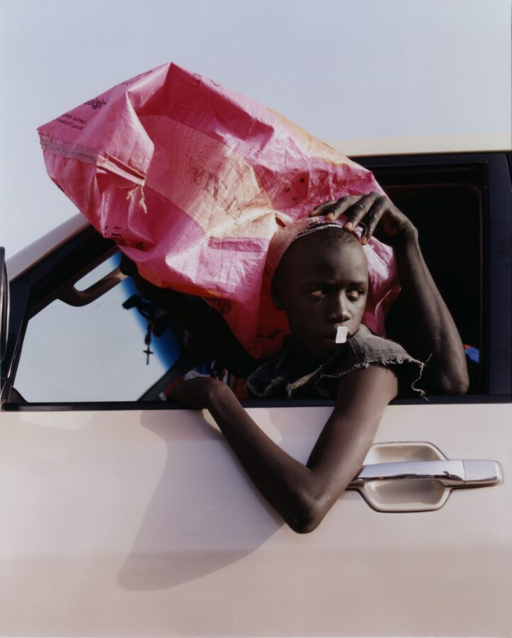 Tirage de Harley Weir presente a l'exposition Fragile Beaute au Jeu de Paume : un jeune passager a la fenetre d'une voiture, un grand sac rose pose sur la tete