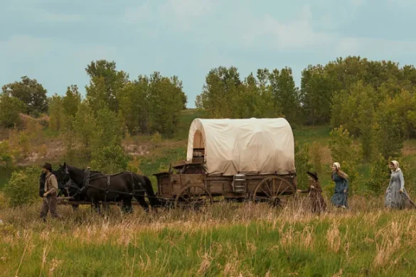Un chariot bâché tiré par des chevaux traverse la prairie, la famille Ingalls à pied, dans la nouvelle adaptation Netflix de La Petite Maison dans la prairie