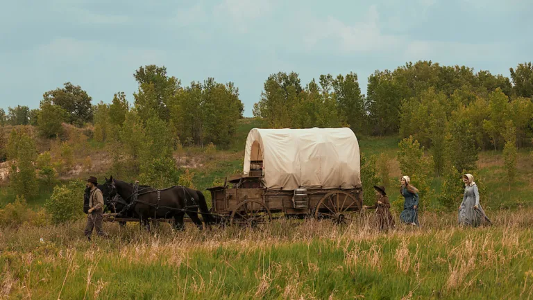 Un chariot bâché tiré par des chevaux traverse la prairie, la famille Ingalls à pied, dans la nouvelle adaptation Netflix de La Petite Maison dans la prairie