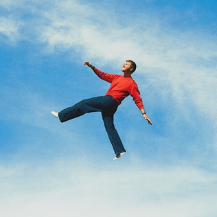 Pochette de l'album Wildchild d'Alex Warren : un homme en pull rouge saute dans un ciel bleu