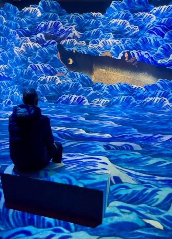 Visiteur assis devant une projection de vagues et d'une carpe géante à l'exposition immersive Passion Japon à la Villette