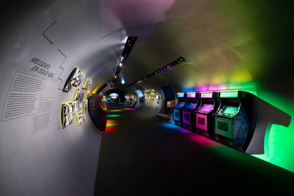 Vue de l'exposition Video Games & Music a la Philharmonie de Paris : bornes d'arcade retro sous des eclairages colores dans un espace en tunnel