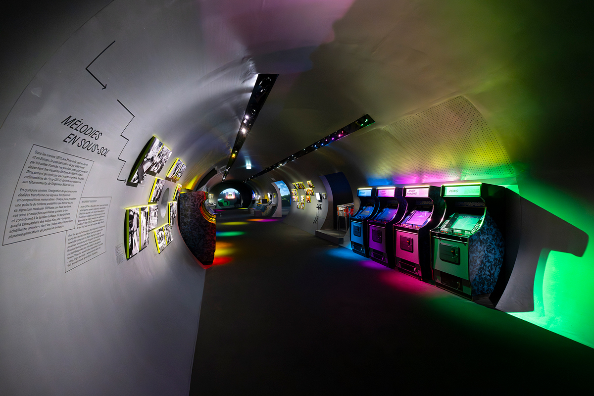Vue de l'exposition Video Games & Music a la Philharmonie de Paris : bornes d'arcade retro sous des eclairages colores dans un espace en tunnel