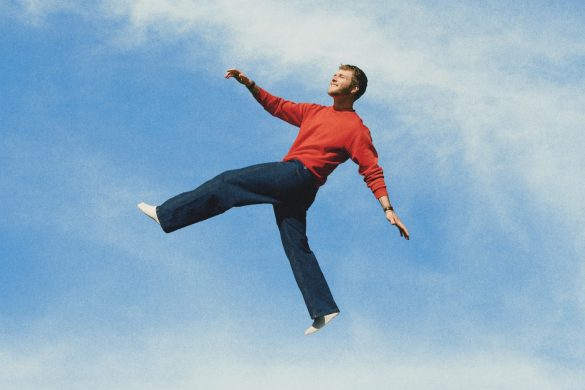 Pochette de l'album WILDCHILD d'Alex Warren : le chanteur flottant dans un ciel bleu, en pull rouge et jean