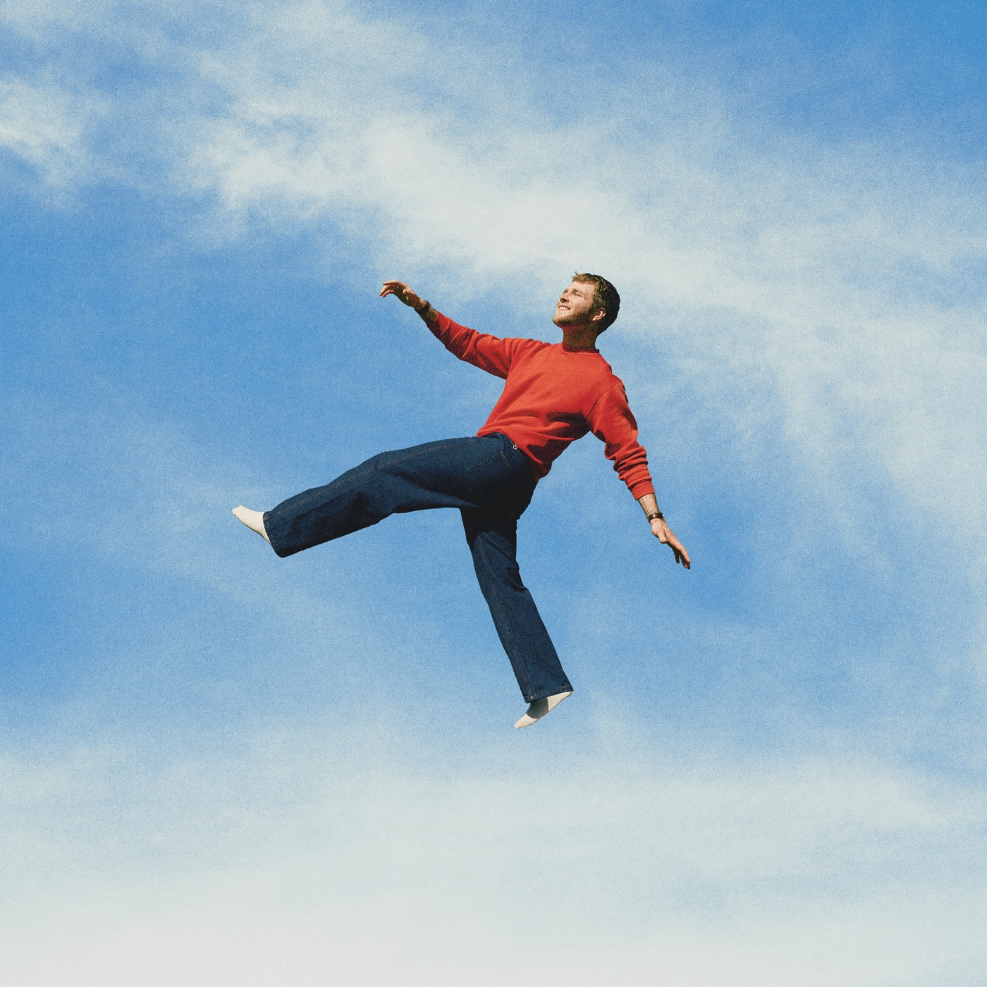 Pochette de l'album WILDCHILD d'Alex Warren : le chanteur flottant dans un ciel bleu, en pull rouge et jean