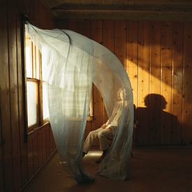 Pochette de l'album Ride Lonesome de Beck : une silhouette assise derrière un voilage dans une pièce en bois baignée de lumière
