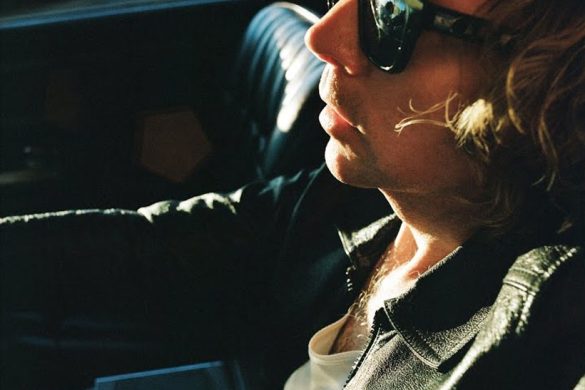 Pochette de l'album Ride Lonesome de Beck, l'artiste de profil, lunettes de soleil, dans une voiture au soleil couchant