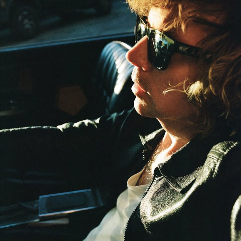 Pochette de l'album Ride Lonesome de Beck, l'artiste de profil, lunettes de soleil, dans une voiture au soleil couchant