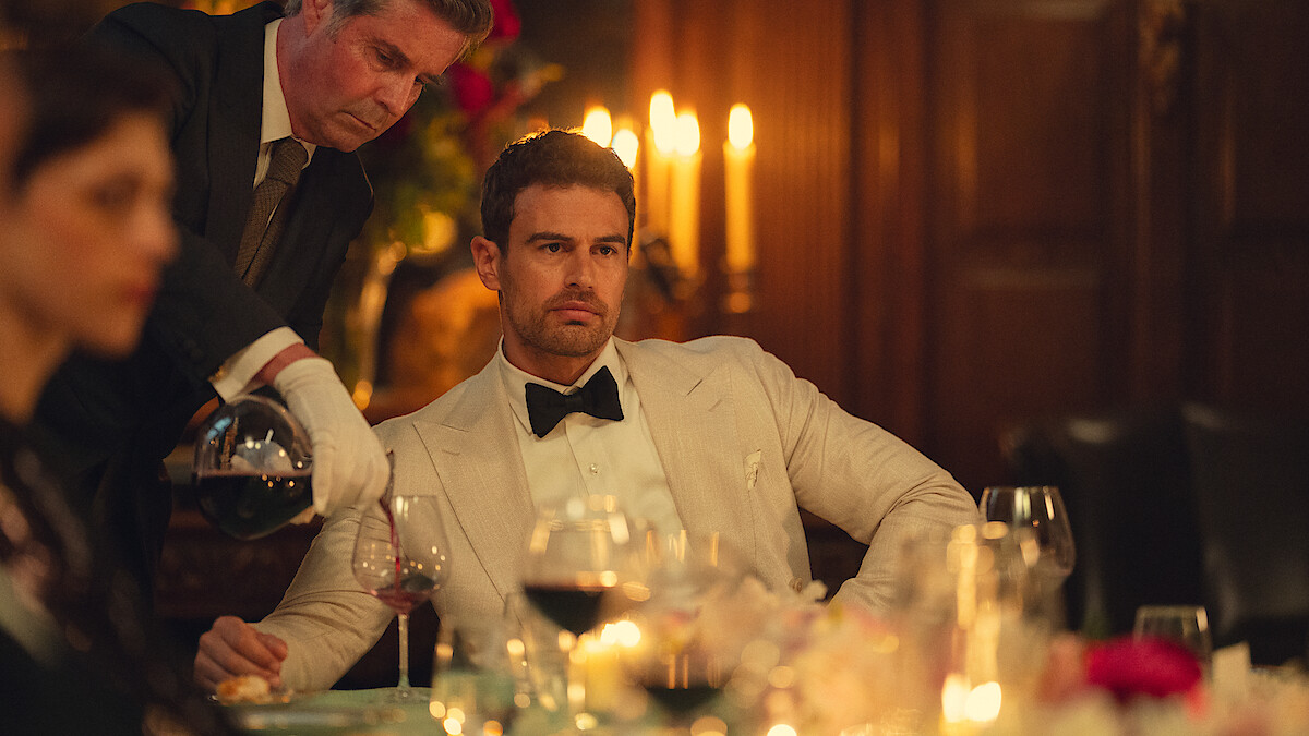 Theo James en costume blanc dans une scène de dîner de The Gentlemen saison 2 sur Netflix