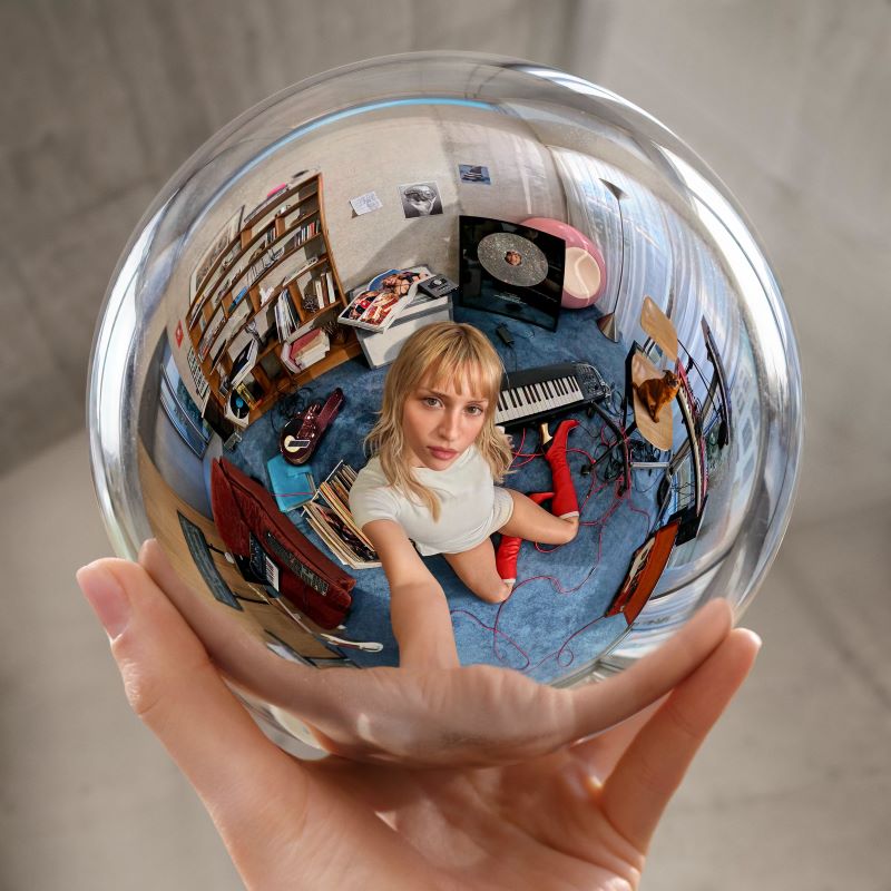 Pochette de l'album Instinct d'Angèle : la chanteuse dans une boule de cristal tenue à bout de bras, clin d'oeil à Escher