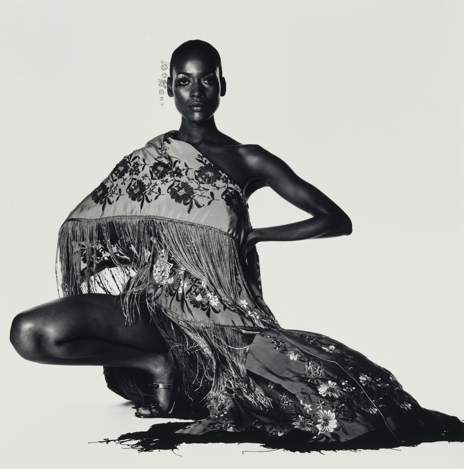 Photographie noir et blanc d'Irving Penn: un mannequin en robe brodée à franges, assis sur fond clair, exposé à la MEP