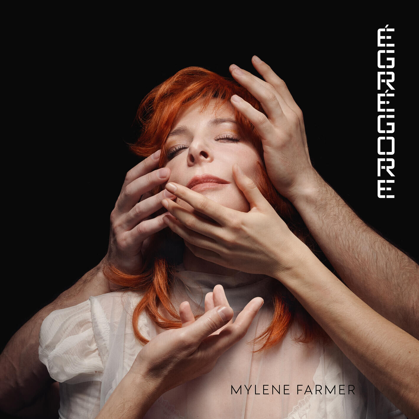 Pochette de l'album Égrégore de Mylène Farmer, visage aux yeux clos entouré de mains, chevelure rousse